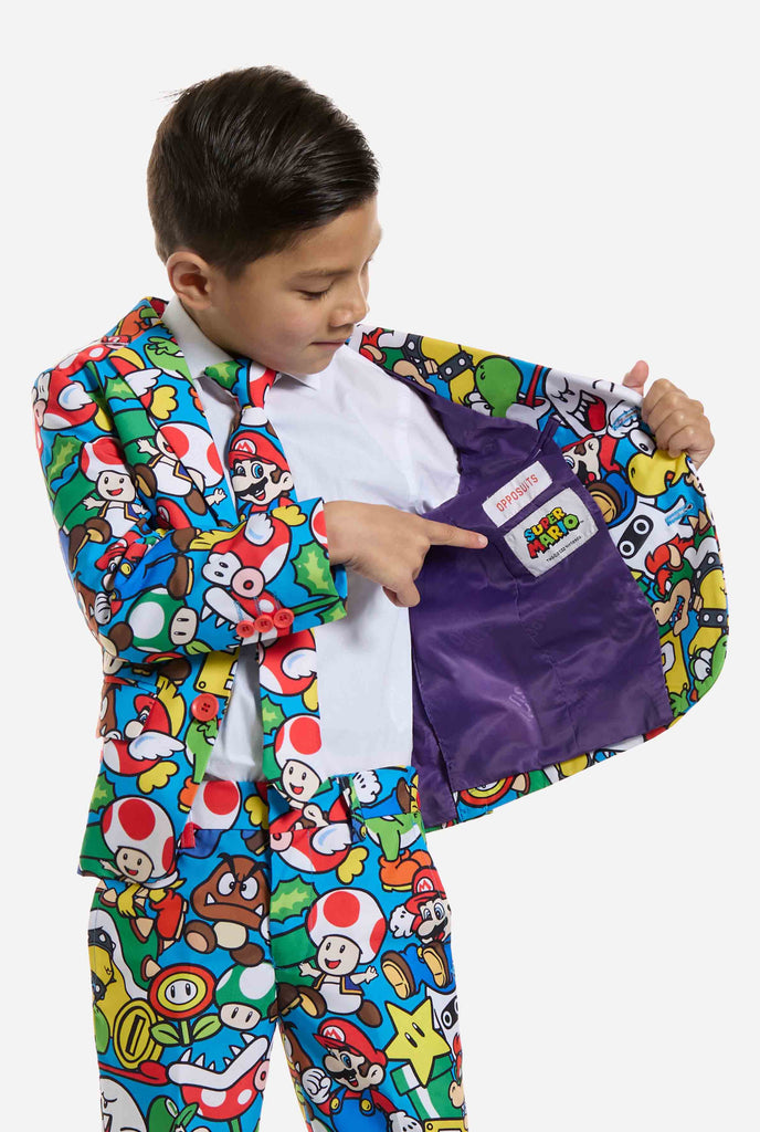 Afbeelding van kind dat een Super Mario all over print pak draagt, bestaande uit blazer, broek en stropdas. Hoofdkleur is blauw, maar er is ook geel, rood en wit.