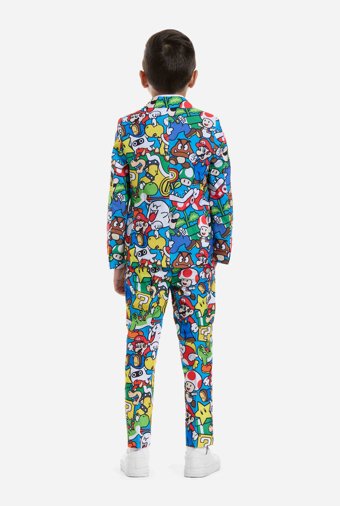 Afbeelding van kind dat een Super Mario all over print pak draagt, bestaande uit blazer, broek en stropdas. Hoofdkleur is blauw, maar er is ook geel, rood en wit.