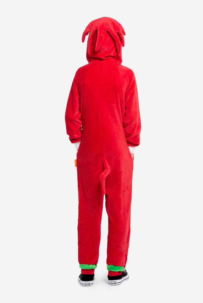 Een kind draagt ​​een felrode kinderonesie met Knuckles the Echidna-thema van OppoSuits. De leuke en knusse onesie heeft een ritssluiting aan de voorkant en een vaste capuchon die lijkt op het gezicht van Knuckles, compleet met expressieve ogen en slappe dreadlocks. Het pak is voornamelijk rood, met een wit halvemaanvormig patroon op de borst, wat de iconische look van Knuckles uit de videogameserie Sonic the Hedgehog weerspiegelt.