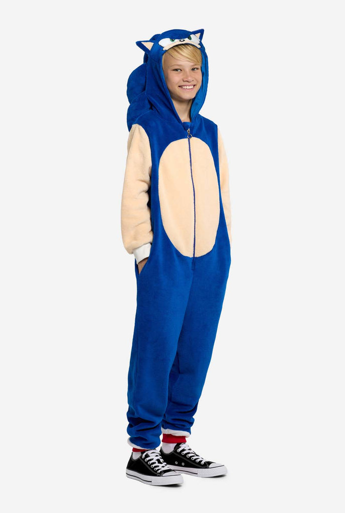 Een kind draagt ​​een blauw en beige Sonic the Hedgehog-thema kinderonesie van OppoSuits. De comfortabele onesie heeft een rits aan de voorkant en een capuchon die is ontworpen om te lijken op Sonics iconische gezicht, compleet met oren en een expressieve blik. Het blauwe lichaam van het pak contrasteert met de beige buik, wat Sonics look nabootst. Deze leuke, comfortabele en stijlvolle onesie is perfect voor loungen, themafeestjes en brengt nostalgische videogame-vibes naar elke gelegenheid.