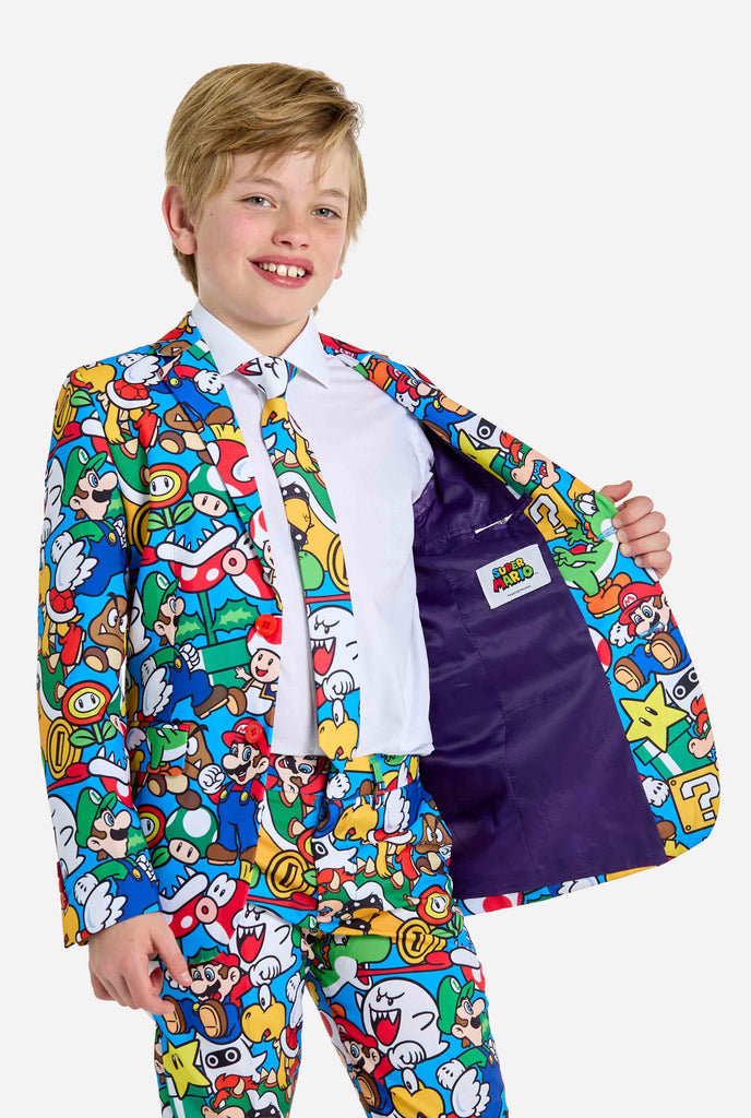 Afbeelding van tiener die een Super Mario all over print shirt draagt, bestaande uit blazer, broek en stropdas. Hoofdkleur is blauw, maar er is ook geel, rood en wit.