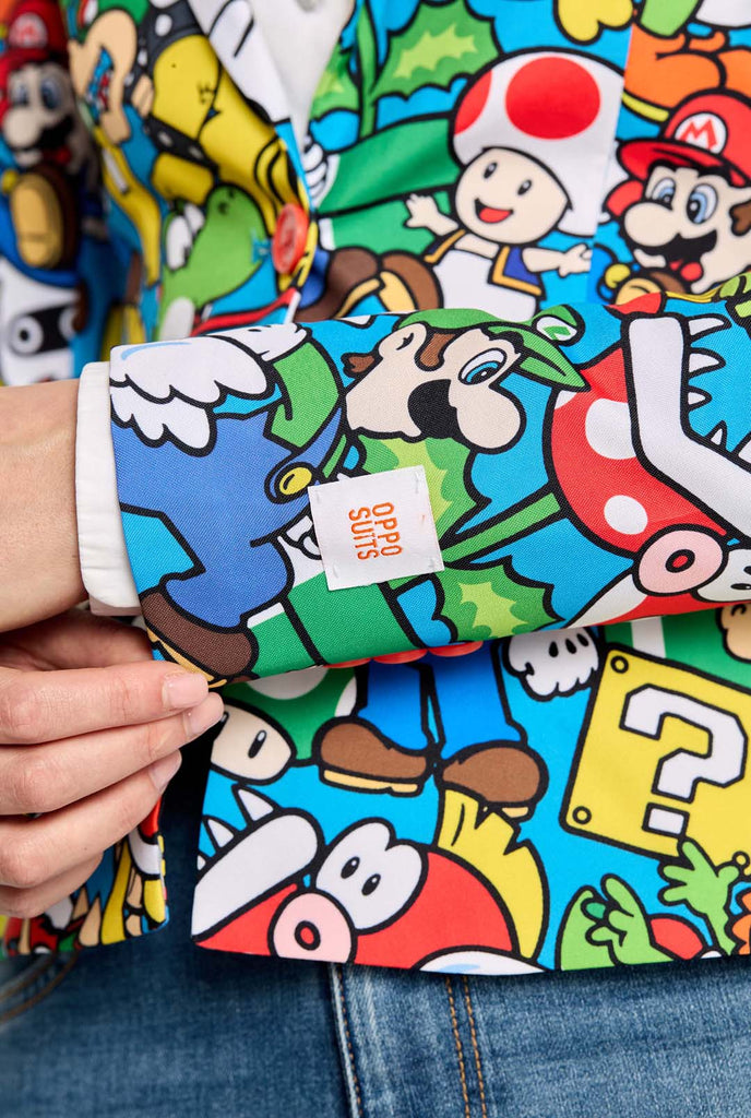 Vrouw draagt ​​een all-over print Super Mario blazer met iconische Super Mario karakters. De basis is lichtblauw, maar er is ook geel, rood en wit.