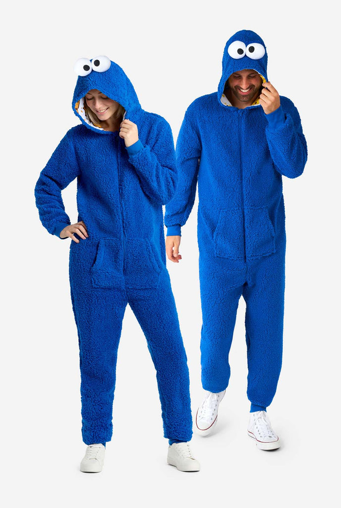 Man en vrouw dragen blauwe pluche Cookie Monster Adult onesie voor volwassenen. Staan naast elkaar, capuchon vasthoudend met één hand.