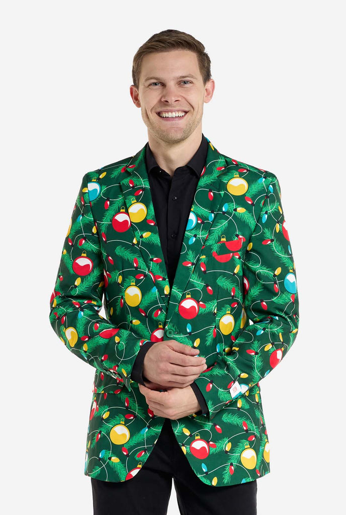 Man wearing green Christmas blazer for men with decorated Christmas tree print. Man also wearing a black pants and black men's shirt.