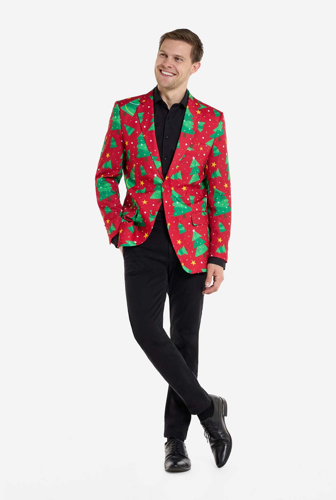 Man wearing red Christmas blazer for men with Christmas trees and stars print. Man also wearing a black pants and black men's shirt. Fill body image.