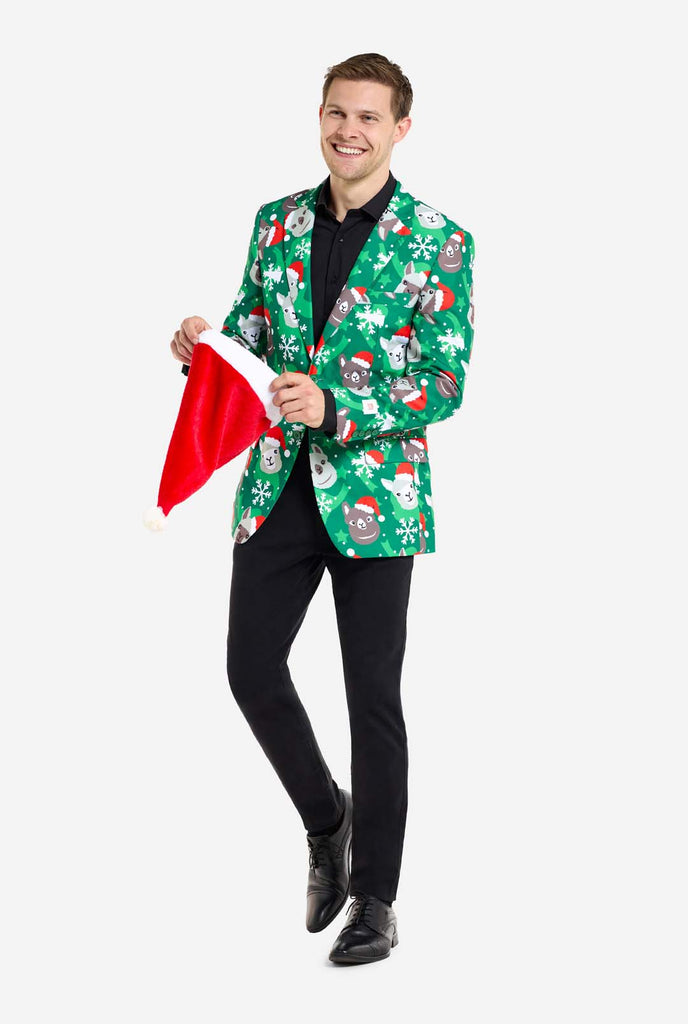 Man wearing green Christmas blazer for men with Christmas llamas. Man also wearing a black pants and black men's shirt. Holding Christmas hat.