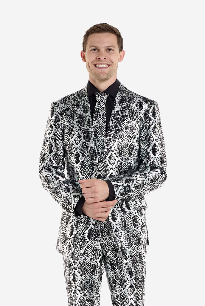 Een man draagt ​​een opvallend zilver-zwart pak met slangenprint van OppoSuits. Het opvallende pak heeft een opvallend slangenpatroon en biedt een strakke, modieuze look, perfect voor feestjes, evenementen of voor het maken van een gedurfd modestatement. Het herenpak wordt gecombineerd met een zwart overhemd en een bijpassende stropdas met slangenprint, wat een verfijnd tintje toevoegt aan het geheel. De zelfverzekerde glimlach en de formele, maar moderne outfit van de man stralen een high-fashion, stijlvol