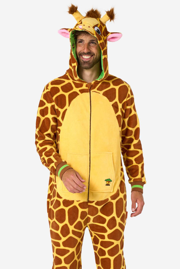 A smiling man is wearing a brown and yellow adult onesie designed as a giraffe. The onesie features a hood resembling a Giraffes head, and giraffe details, perfect for cozy lounging or costume parties.