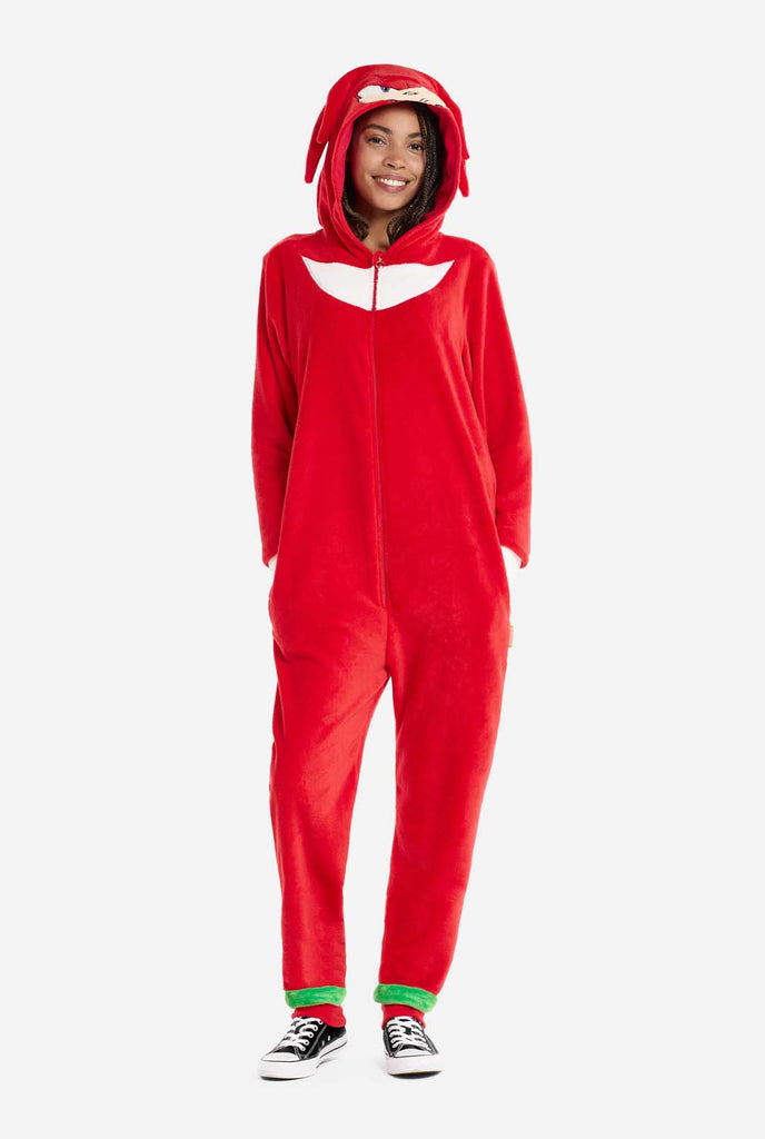 Een vrouw draagt ​​een felrode Knuckles the Echidna onesie voor volwassenen, een gezellige en speelse outfit geïnspireerd op het beroemde personage uit de Sonic the Hedgehog-serie. De onesie is voorzien van de kenmerkende witte borstpatch van Knuckles en heeft een capuchon die het gezicht van Knuckles laat zien, compleet met zijn expressieve ogen en lange rode dreads.