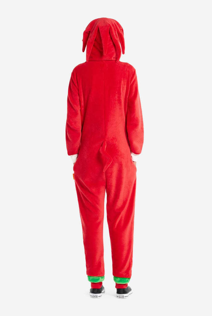 Een vrouw draagt ​​een felrode Knuckles the Echidna onesie voor volwassenen, een gezellige en speelse outfit geïnspireerd op het beroemde personage uit de Sonic the Hedgehog-serie. De onesie is voorzien van de kenmerkende witte borstpatch van Knuckles en heeft een capuchon die het gezicht van Knuckles laat zien, compleet met zijn expressieve ogen en lange rode dreads. Beeld van de achterkant.