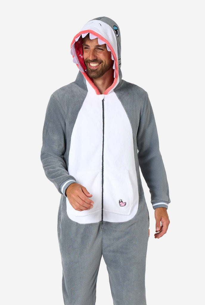 A man is wearing a grey and white shark adult onesie featuring playful hood details and cozy, soft material, perfect for lounging or costume events.  The man is smiling and looking side ways.