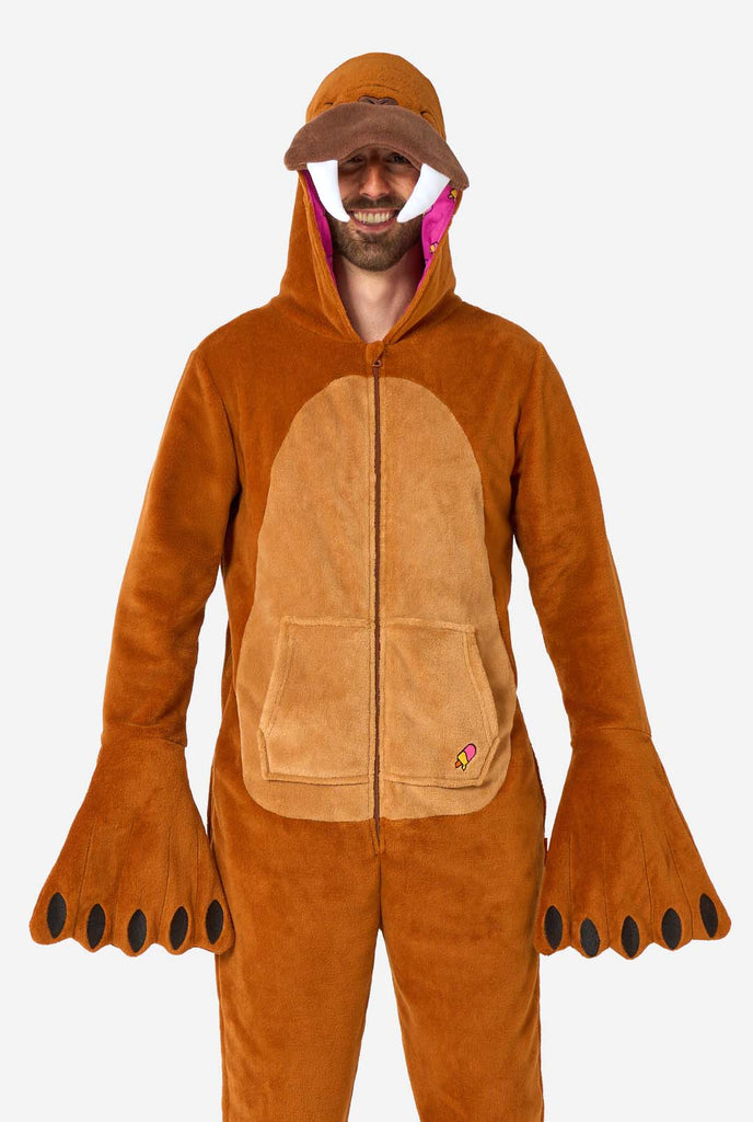 A cheerful man wearing a brown adult onesie designed as a walrus. The onesie features a hood with fangs, stitched gloves resembling paws, and playful walrus details, perfect for cozy lounging or costume parties.