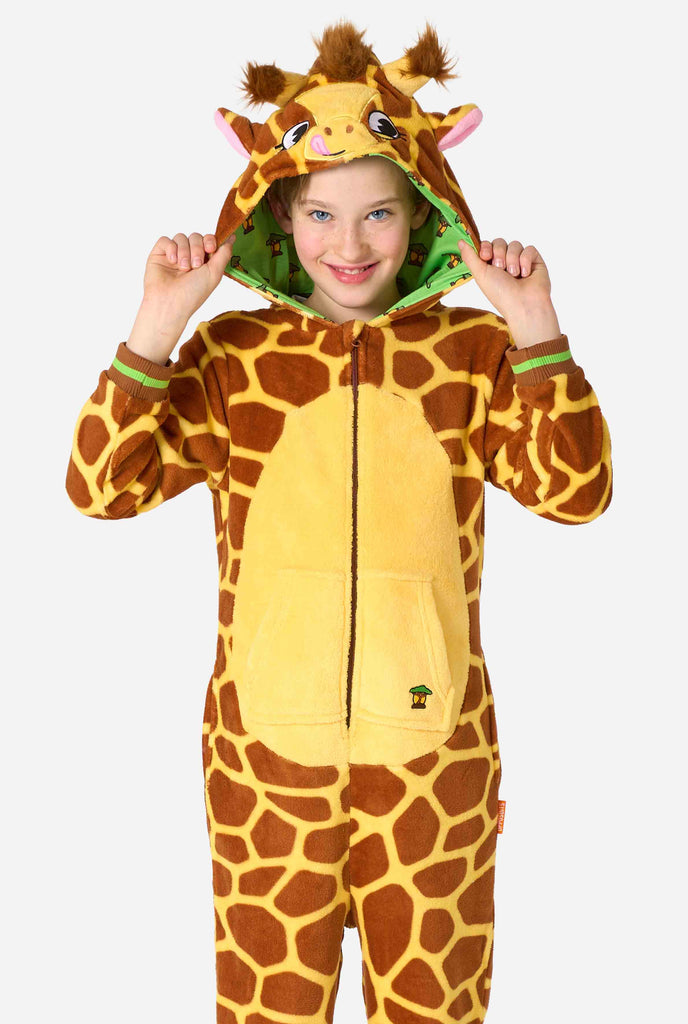 Een lachend kind draagt ​​een bruin en geel kinder onesie ontworpen als een giraffe. De onesie heeft een capuchon die lijkt op het hoofd van een giraffe.