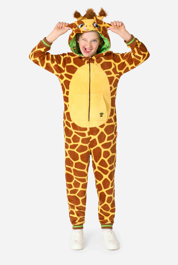 Een lachend kind draagt ​​een bruin en geel kinder onesie ontworpen als een giraffe. De onesie heeft een capuchon die lijkt op het hoofd van een giraffe.