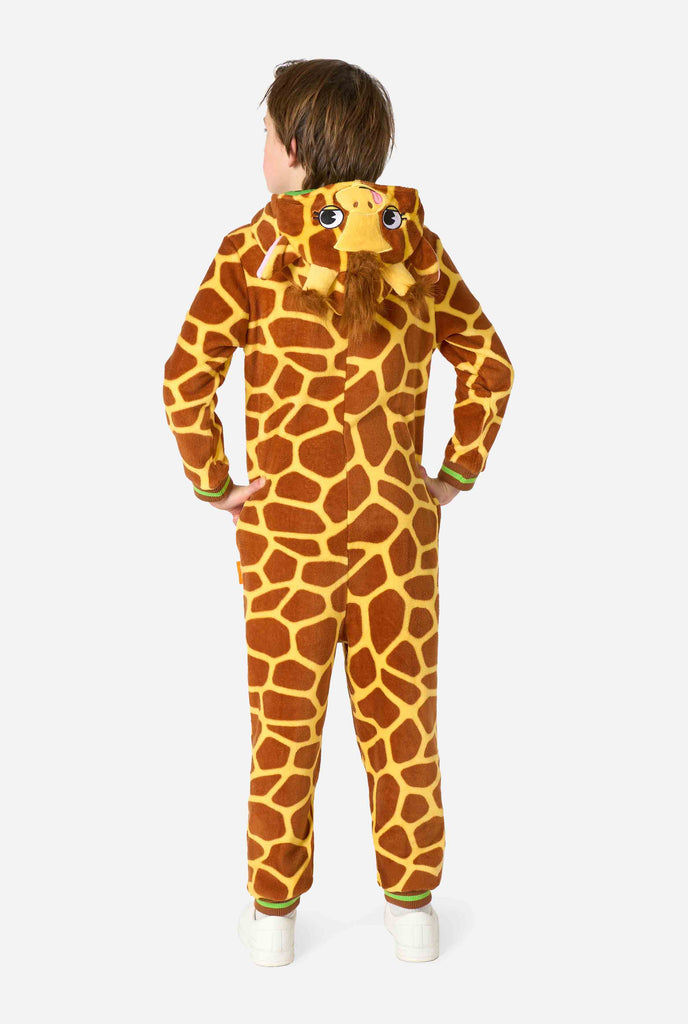 Een lachend kind draagt ​​een bruin en geel kinder onesie ontworpen als een giraffe. De onesie heeft een capuchon die lijkt op het hoofd van een giraffe.