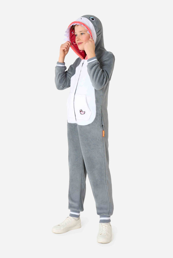 A kid is wearing a grey and white shark kids onesie featuring playful hood details and cozy, soft material, perfect for lounging or costume events. Full body image.